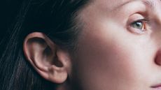 A close up of the right ear of a woman with hazel eyes and long dark hair. 