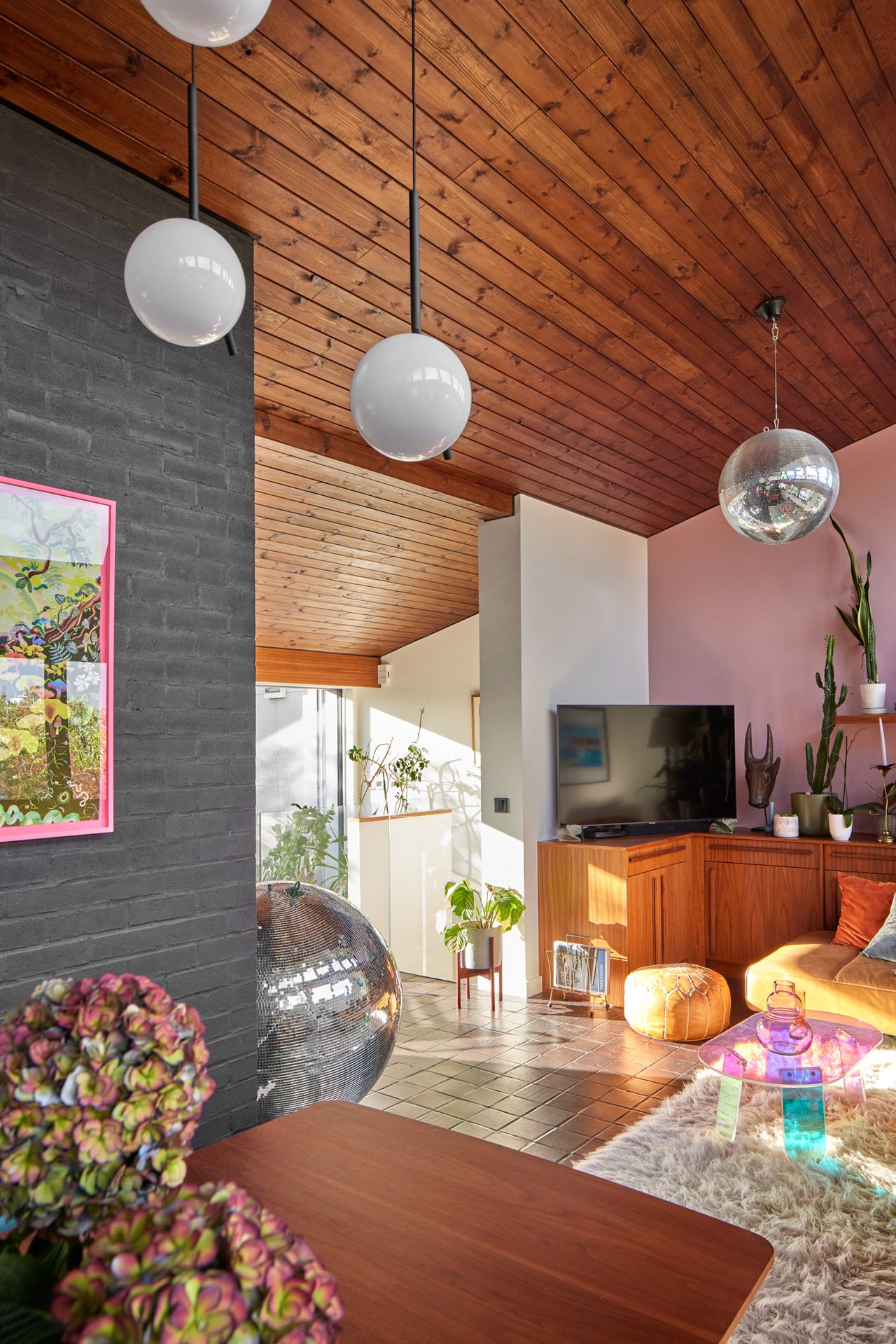 A living room with pendant lights and a disco ball, tiled floors, a brick wall painted grey, a faux fur rug and modernist furniture