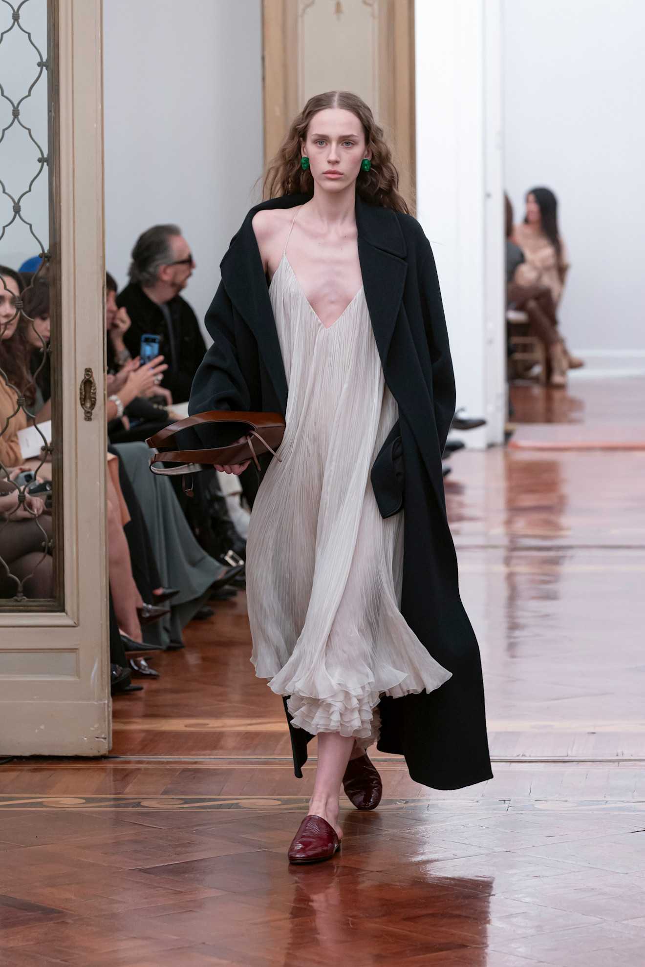 model on Alberta Ferretti Fall 2025 runway wearing red leather slippers, a white sheer dress, and black coat