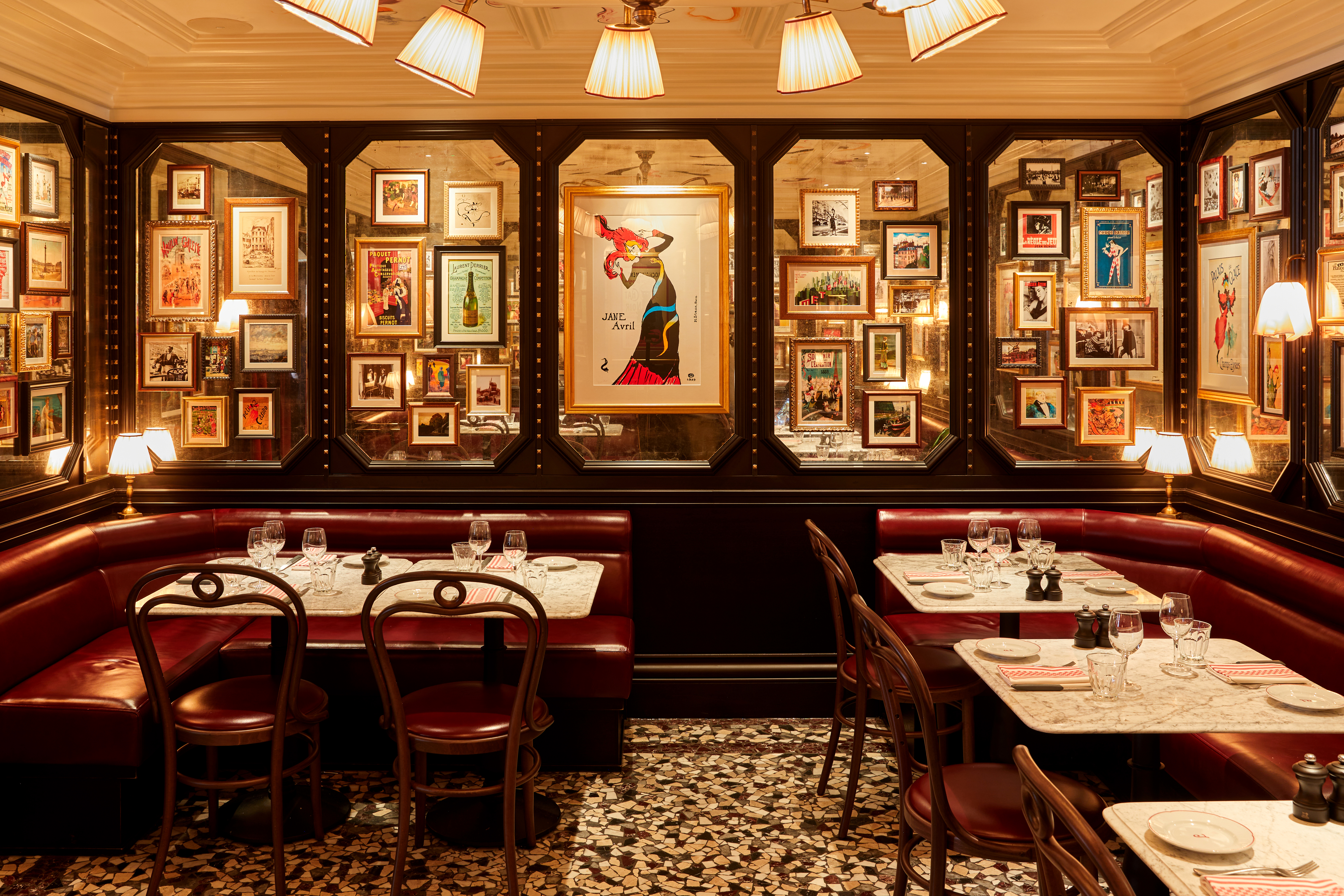 A series of images capturing the timeless interiors of a French-style bistro, filled with uniquely framed artworks, handpainted murals, golden-lit table lamps, wooden furniture, red velvet banquettes, food, and more.