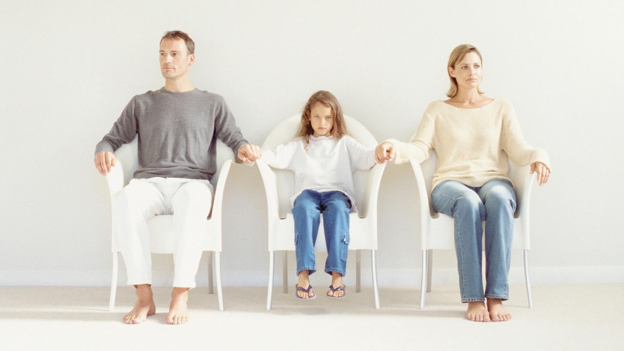 A man and a woman hold their daughter&amp;#039;s hands and stare off into the distance.