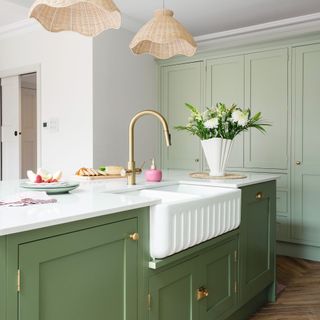 green kitchen island unit with sink and gold boiling tap, next to tall kitchen cabinets in green