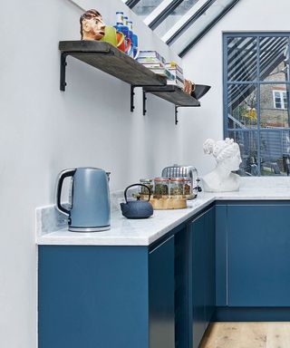 blue kitchen with white worktops, open shelving and kettle and toaster