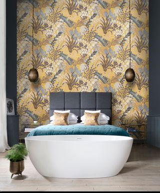 contemporary bedroom with yellow patterned floral wallpaper behind bed, gray fabric upholstered headboard, freestanding bathtub at foot of the bed, wooden flooring