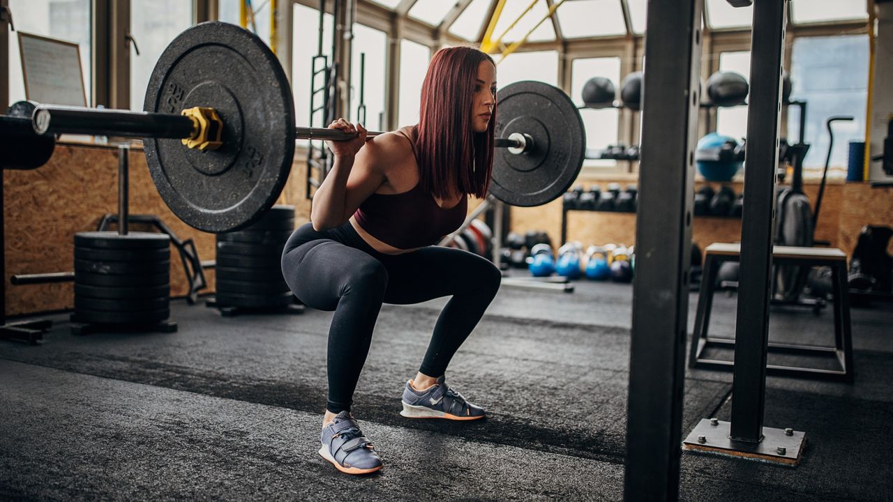 woman in a gym squating with a barbell and weights on her back. 