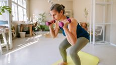 Woman performing a squat while holding dumbbells, in a domestic setting
