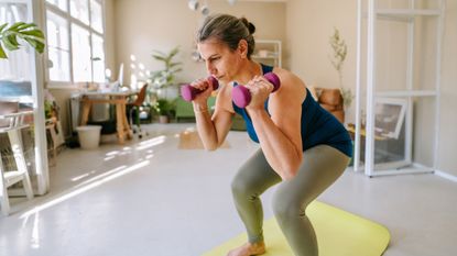 Woman performing a squat while holding dumbbells, in a domestic setting
