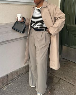 @nnennaechem wearing striped top, tailored trousers, trench and running shoes