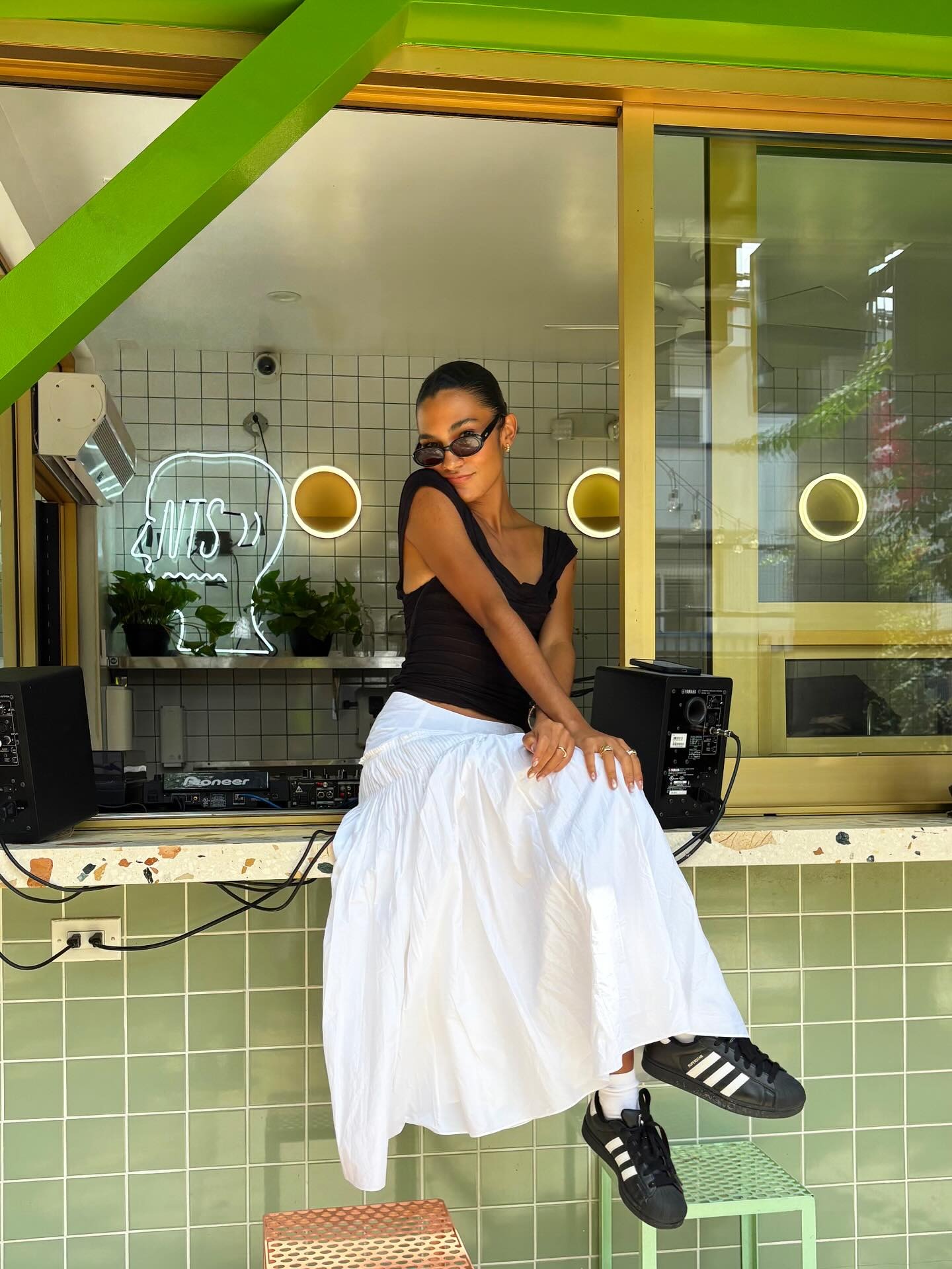 Singer Olivia Dean sat on the table, wearing a white cotton skirt with a black sleeveless top.
