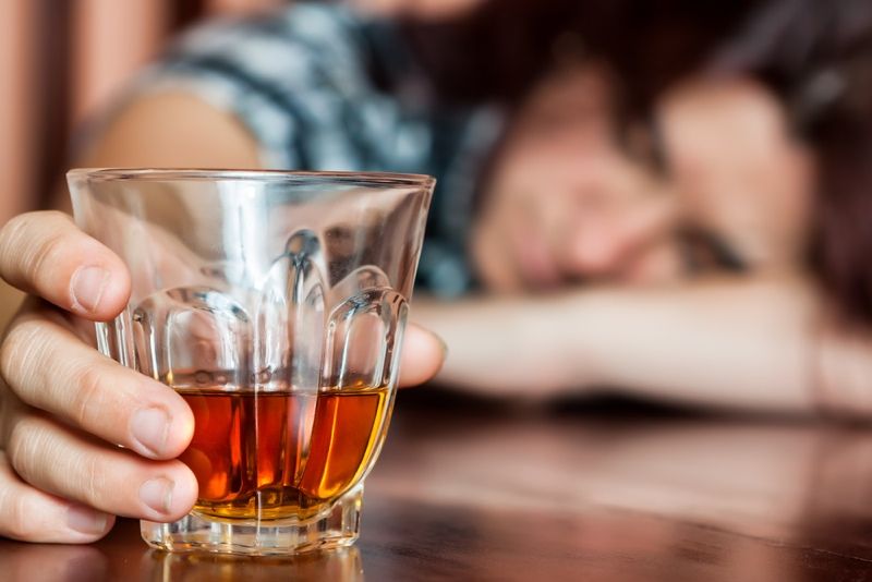 Drunk woman holding an alcoholic drink and sleeping with her head on the table