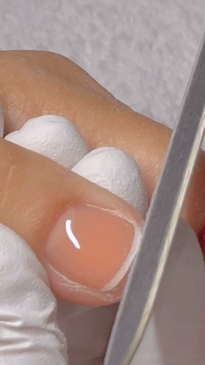 A nail tech filing a nail painted with a peachy base and a white French tip