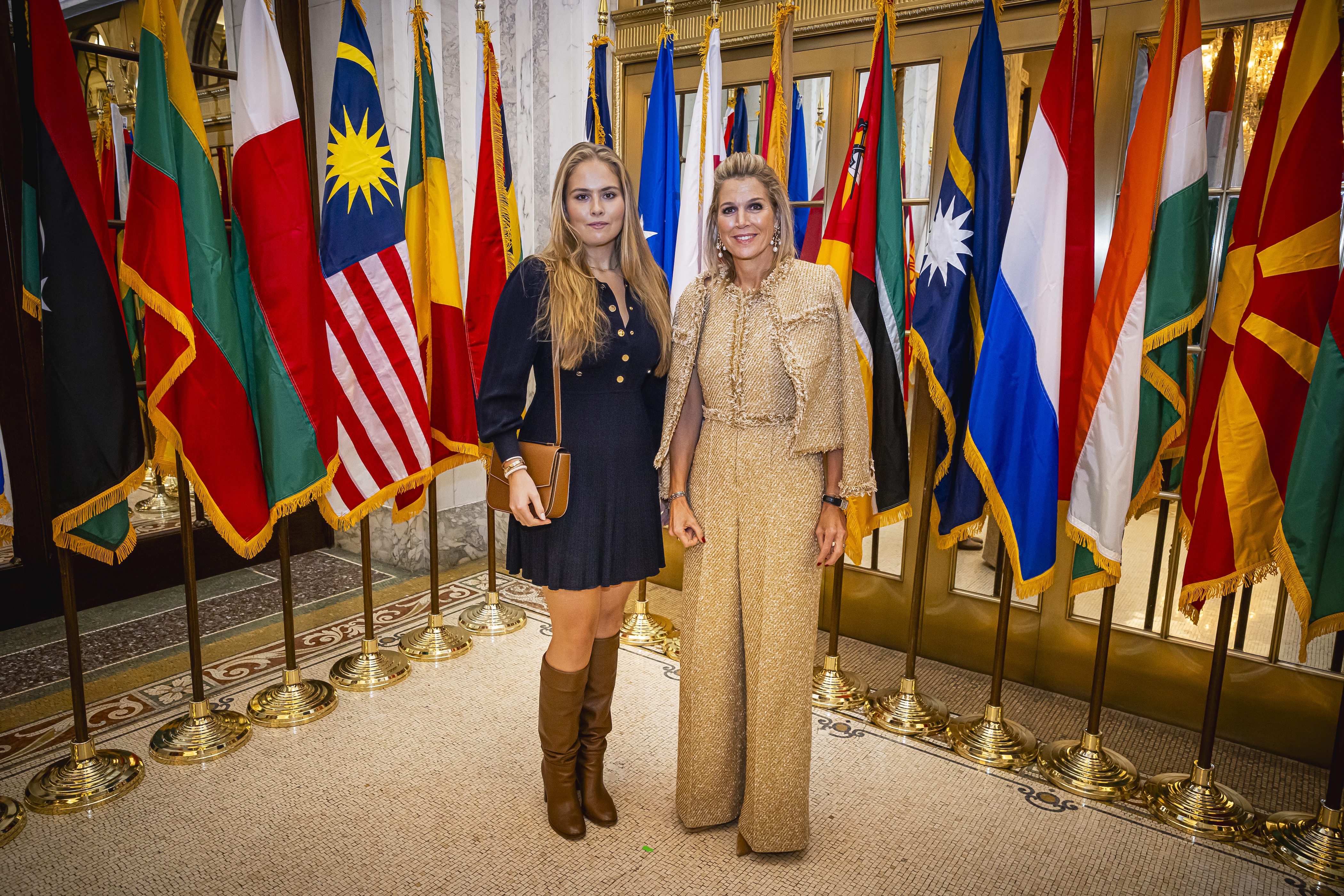 Queen Maxima styles a Me+Em jacket a jumpsuit, standing in front of flags with Princess Catharina-Amalia