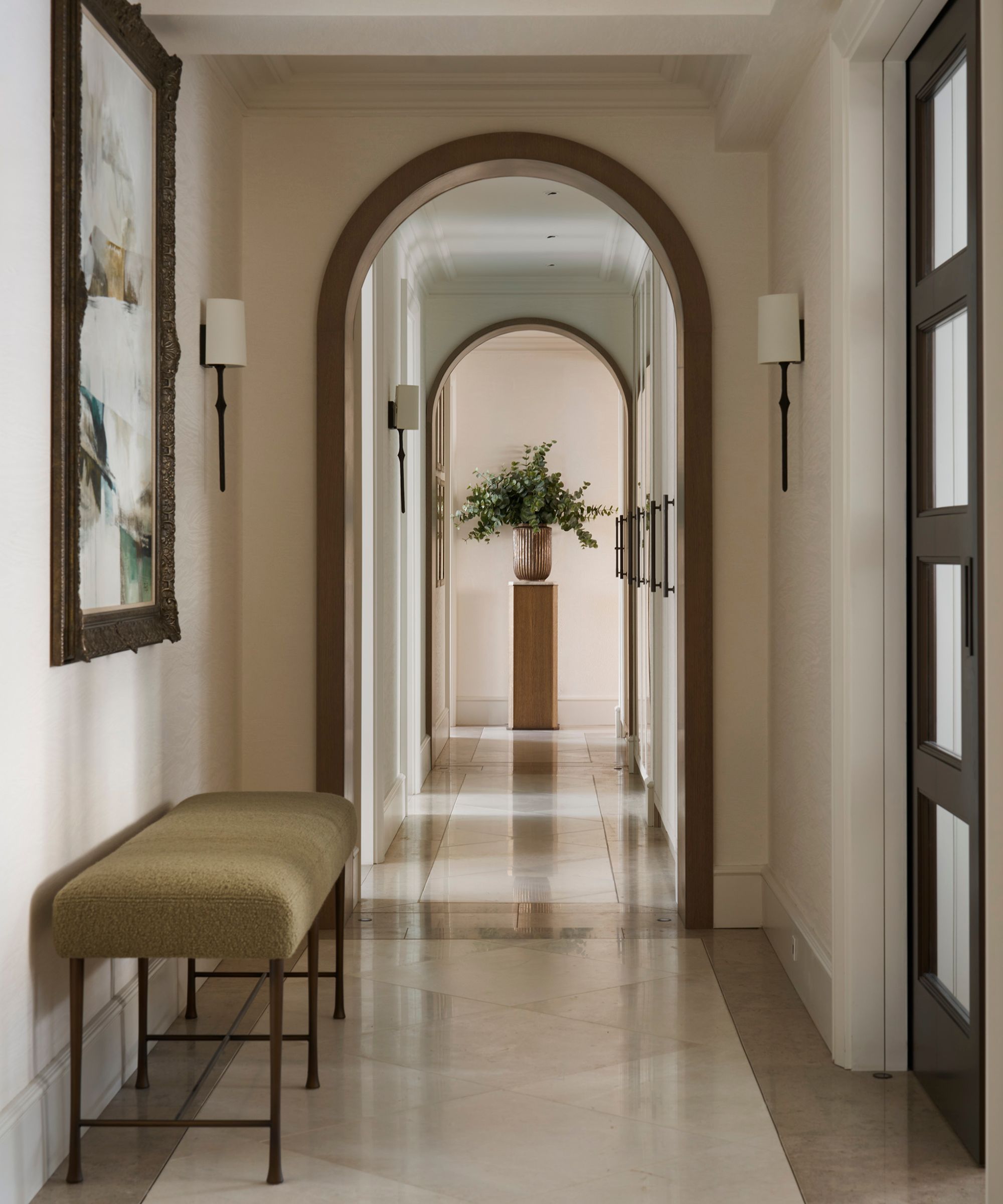 a neutral entryway into a london apartment with arched openings, a tiled floor, and an olive green and iron bench