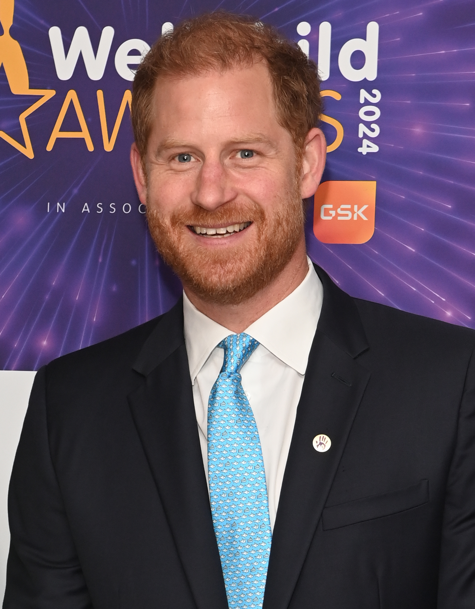 Prince Harry smiling in front of a purple WellChild background