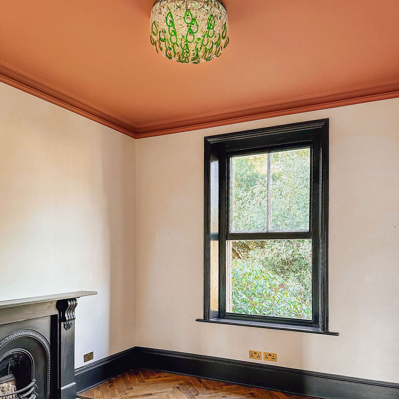 Unfinished home office with white walls, black window frame, terracotta ceiling and green and glass chandelier
