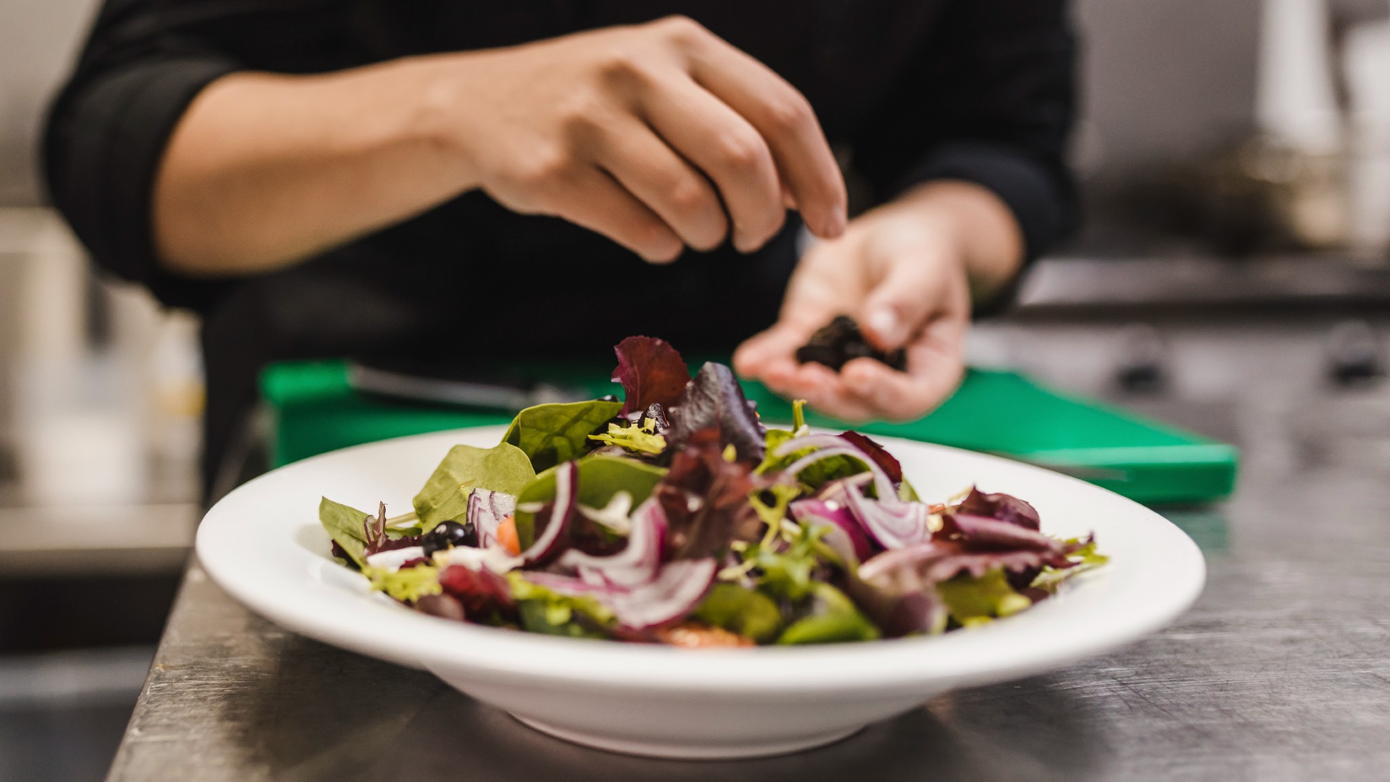Close-up of hands preparing a salad in a bowl on a countertop