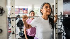 Woman lifting barbell in gym with support from friend from behind