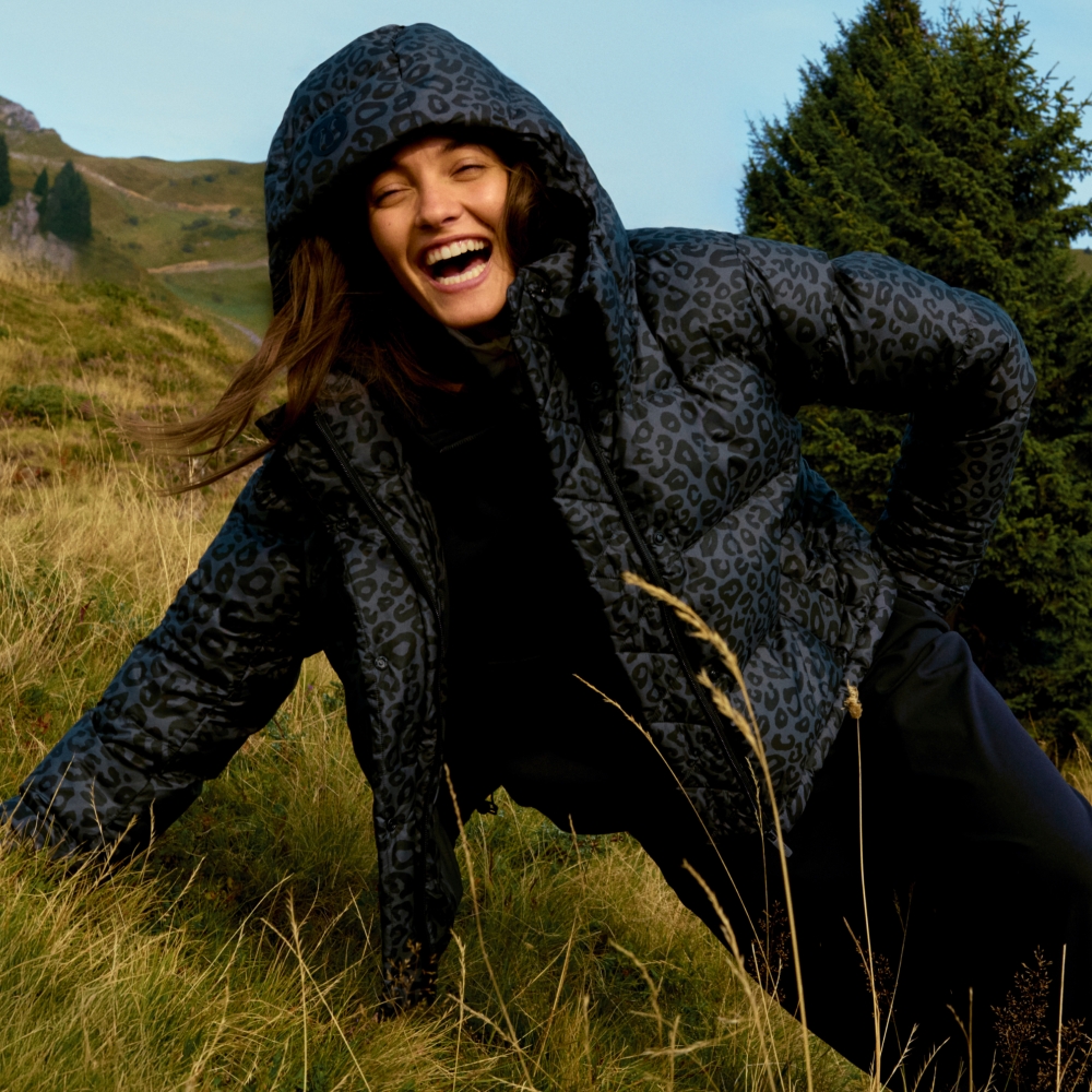 A model leaning on a grassy hill wearing a lululemon leopard print puffer coat