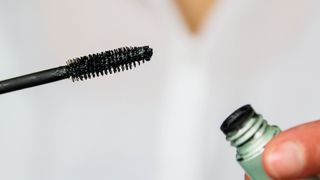 person holding mascara wand and tube