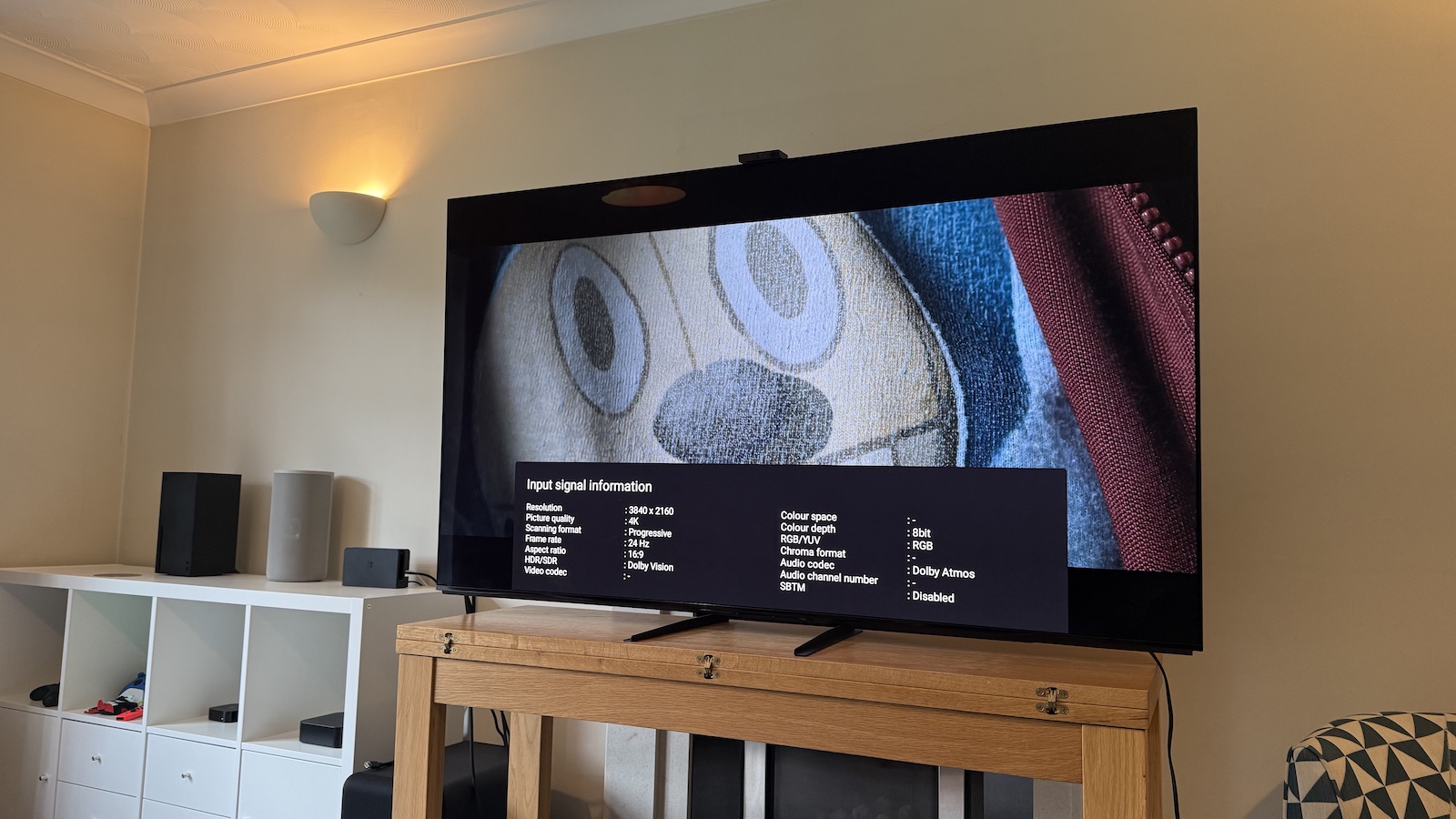 A photo of the 65-inch Sony A95L on a wooden stand in a living room. On the screen is an image from The Electric State from Netflix, with the TV's Input Signal Information menu overlaid.
