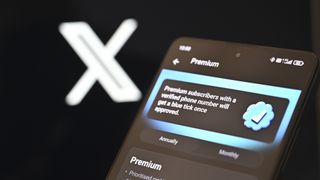 A phone showing the premium subscription menu in the Twitter/X mobile app. The screen reads, "Premium subscribers with a verified phone number will get a blue tick once approved." The X logo is visible behind.