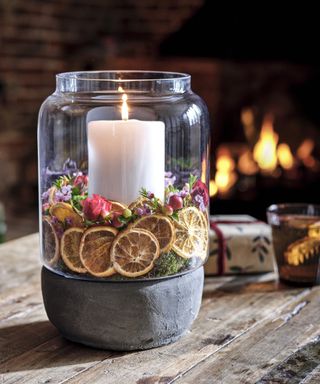 Candle centerpiece in glass jar surrounded by orange slices and flowers