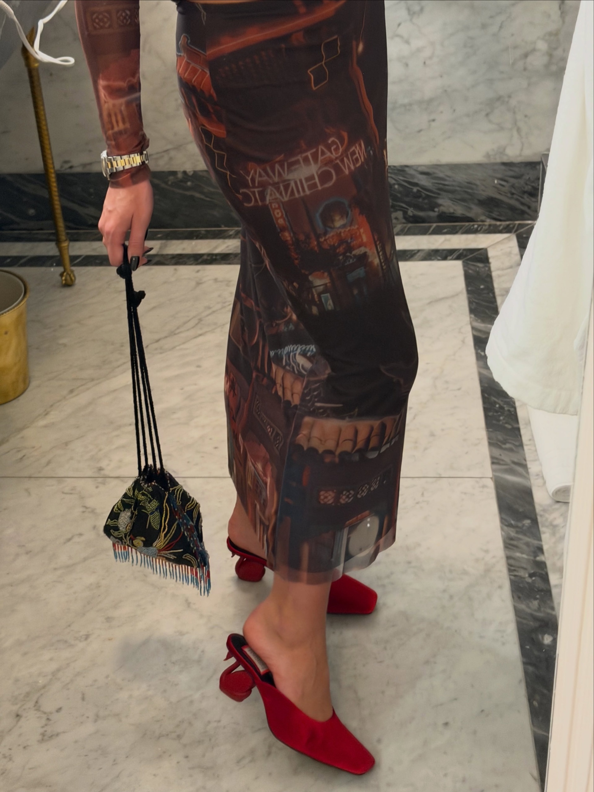 A close up image of an influencer wearing a print dress and holding a print cinched handbag wearing artistic red shoes with sculptural swan heels