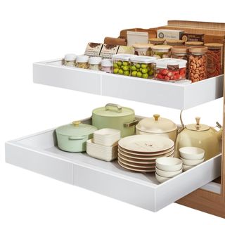 White pull out storage shelves filled with plates, bowls, pans, a tea pot and various dried foods in clear glass and plastic canisters