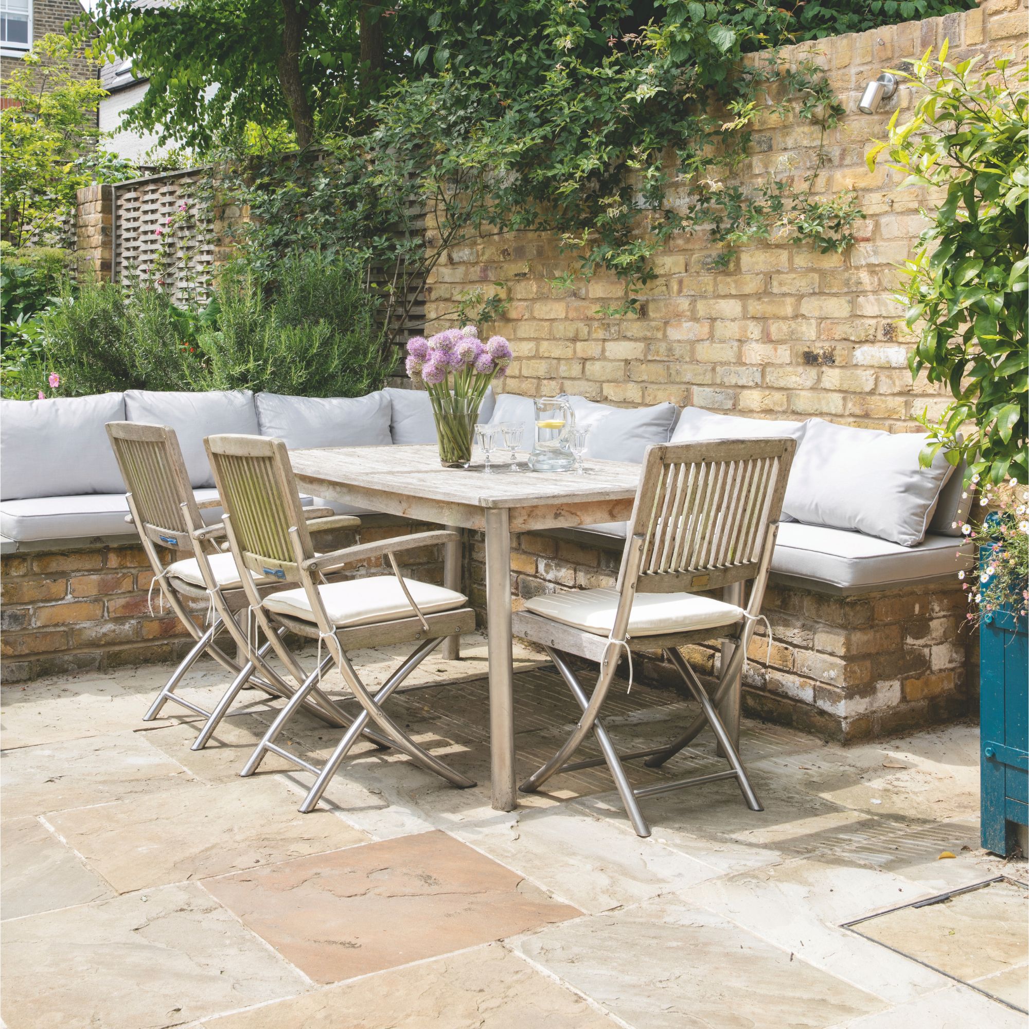 Wooden garden furniture on natural stone patio surrounded by bricked seating area and brick wall