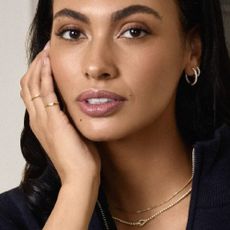 A model wearing gold layered necklaces, and matching gold hoops, and gold rings, all from Zales. 