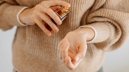 woman wearing cashmere jumper spraying perfume on wrist - best winter perfumes