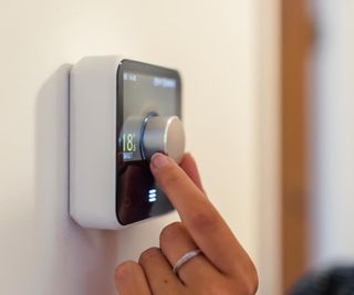 A person adjusting a smart hive thermostat on a wall