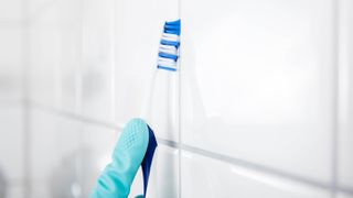 A toothbrush cleaning the grout between tiles
