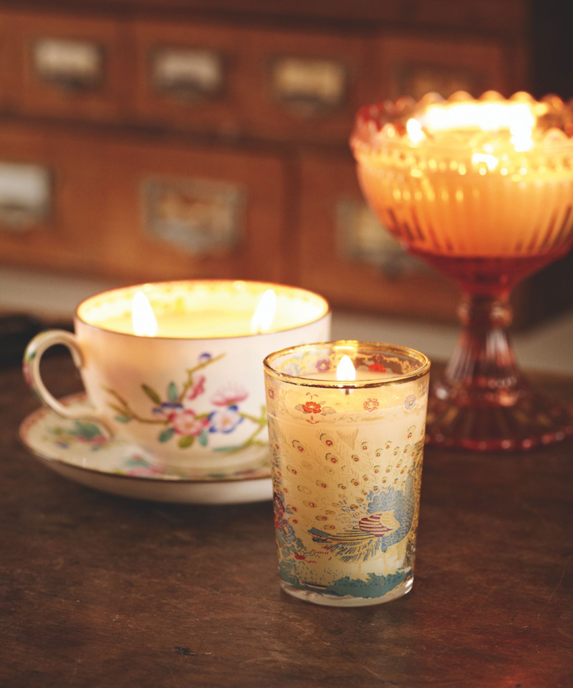 A lit decorative candle with a white floral teacup