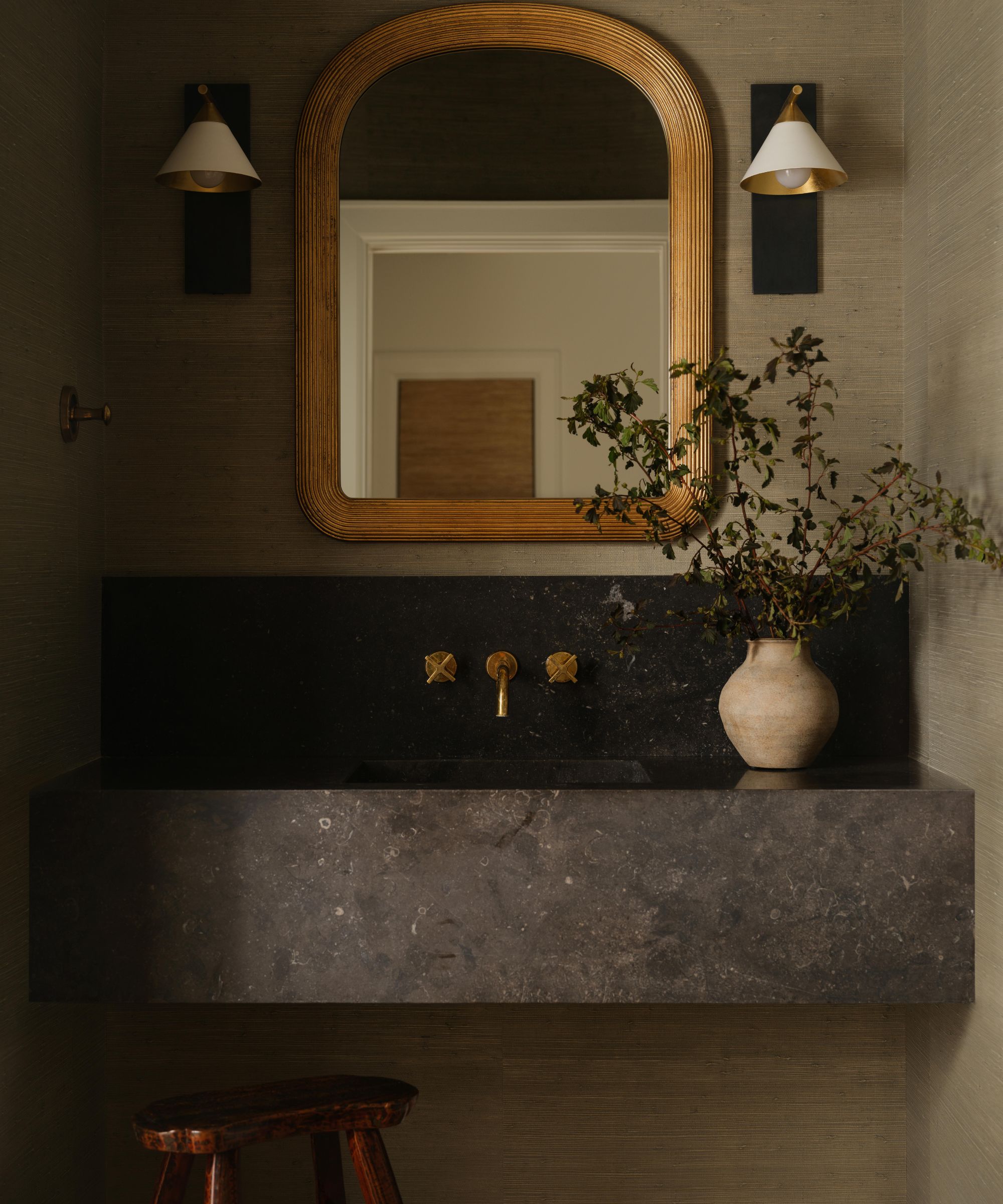 a glasscloth wrapped powder bathroom with large dark marble floating sink, wooden mirror and brass accents
