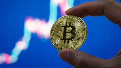 A photo mockup of a hand holding a Bitcoin piece. 