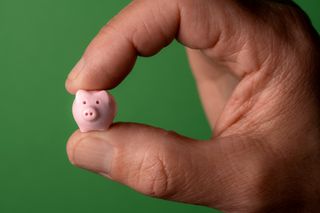 Man's hand pinching tiny ceramic piggy bank between index finger and thumb