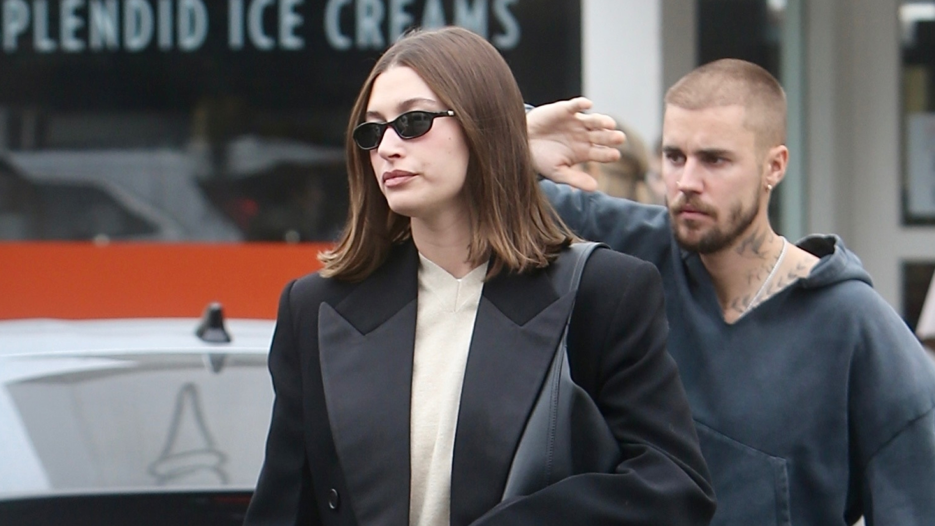 Hailey Bieber wears gray sweatpants and black slippers with a long winter coat and carries a black leather oversize bag as she grabs lunch with husband Justin Bieber