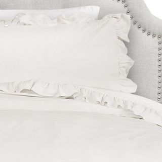 A ruffled white bedding set on a gray headboard
