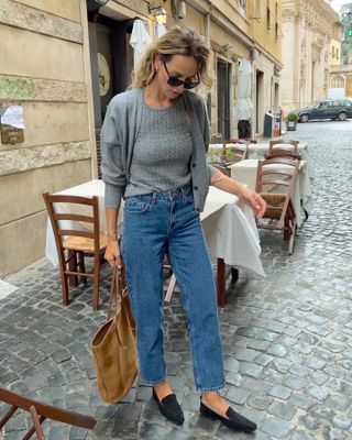 Fashion influencer Anouk Yve posing in a spring outfit with a gray sweater set jeans and loafers