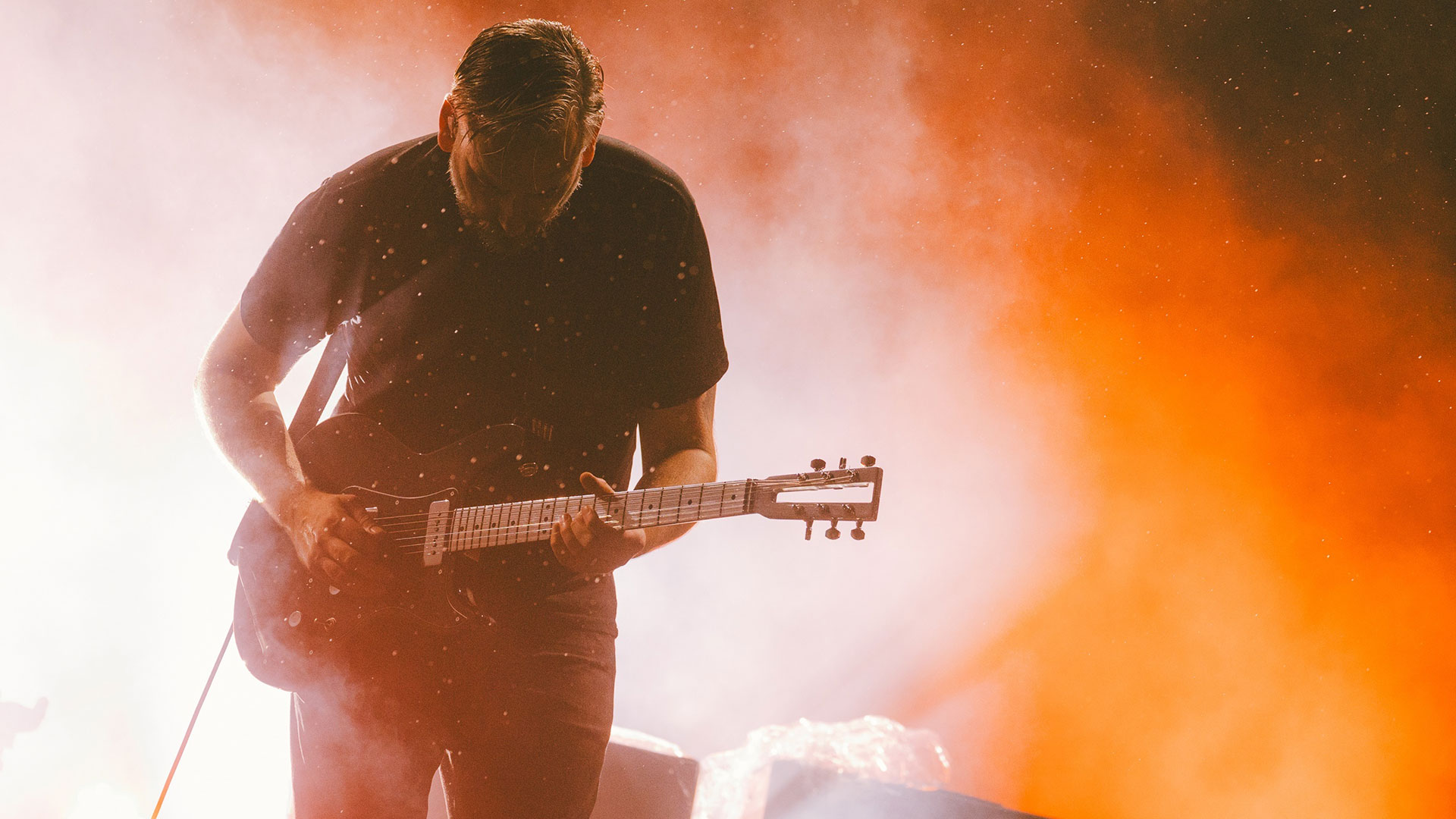 We Lost The Sea guitarist Matthew Harvey onstage against an orange light and dry ice