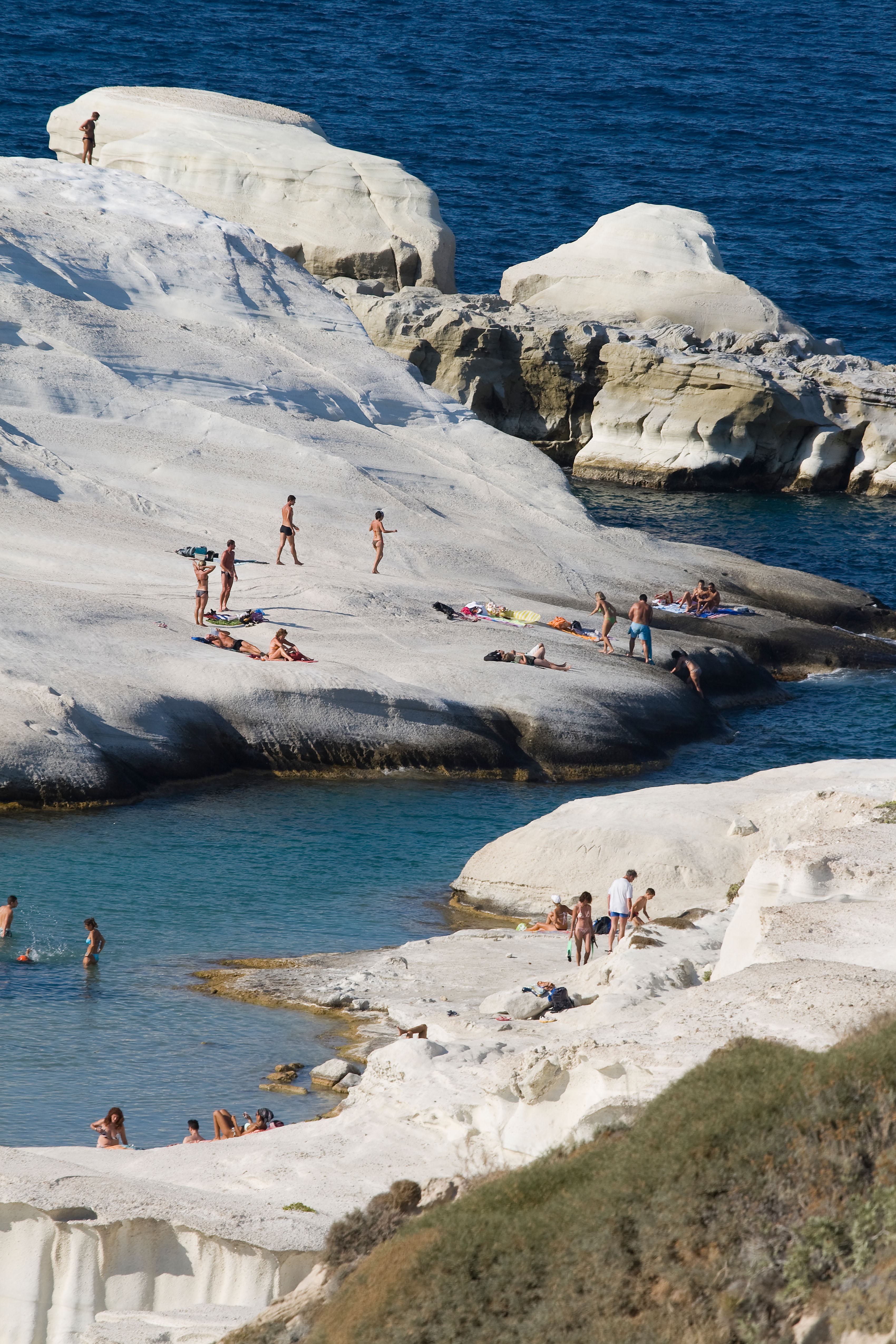 Beach goers walking across white, lunar-like cliffs, next to the sea in Greece