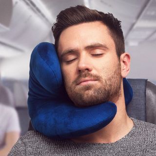 A bearded man uses the J-Pillow on an airplane