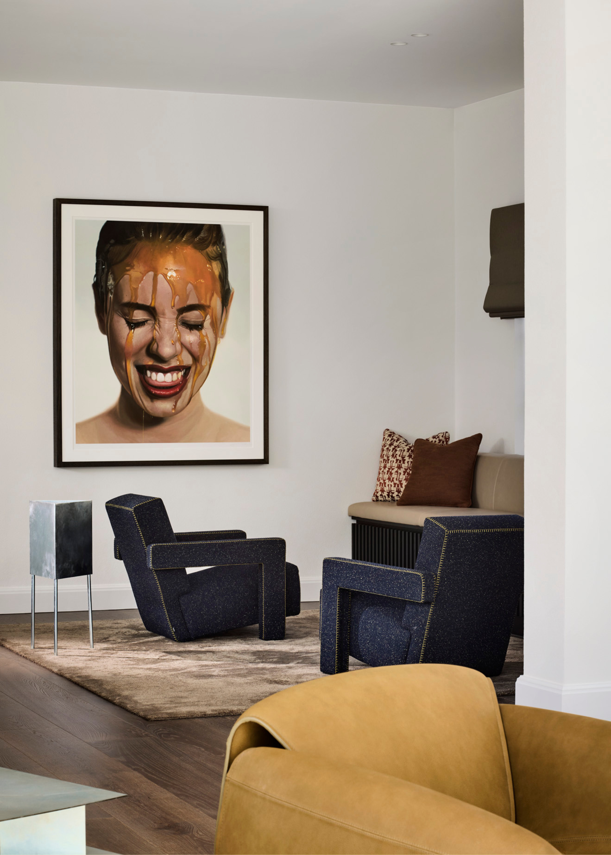 A living room with navy armchairs, a chrome side table, a brown rug, and a beige sofa by a hyper-realistic painting