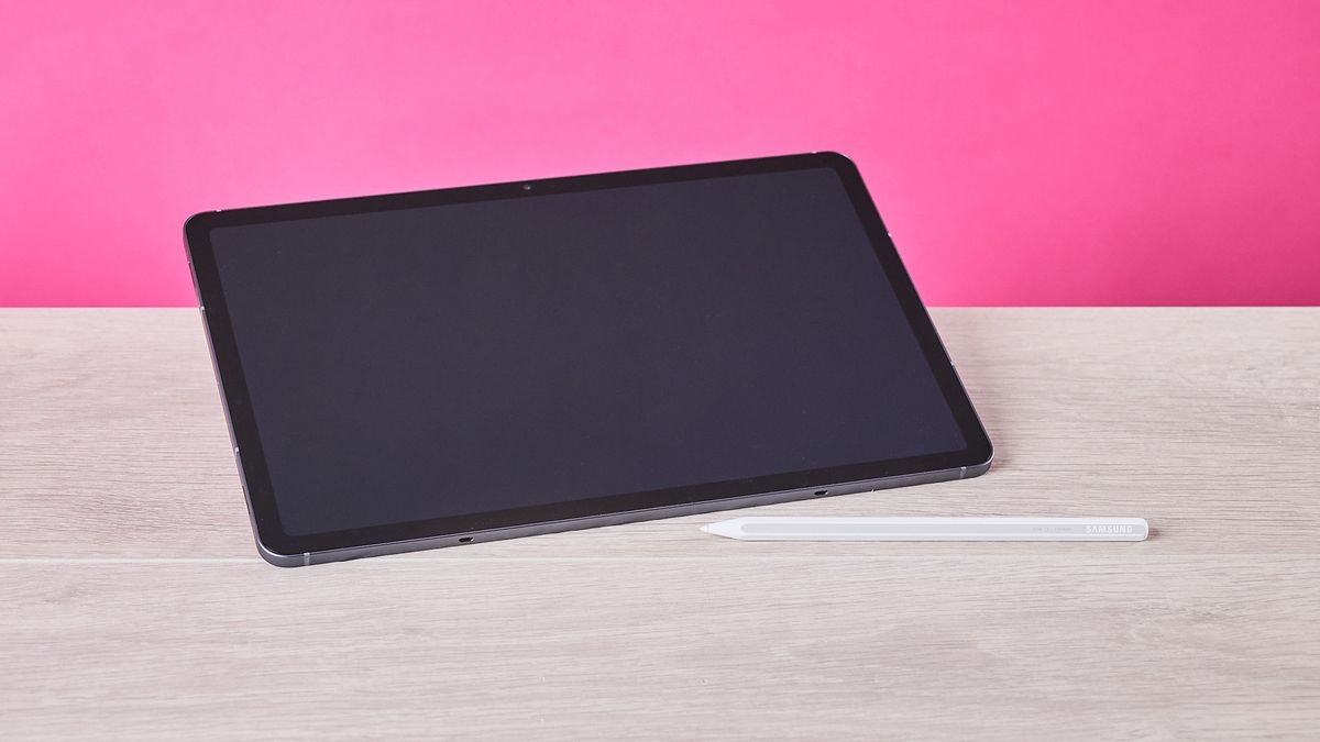 Three-quarter view of Samsung Galaxy Tab S11 and S Pen on a desk with pink wall in background