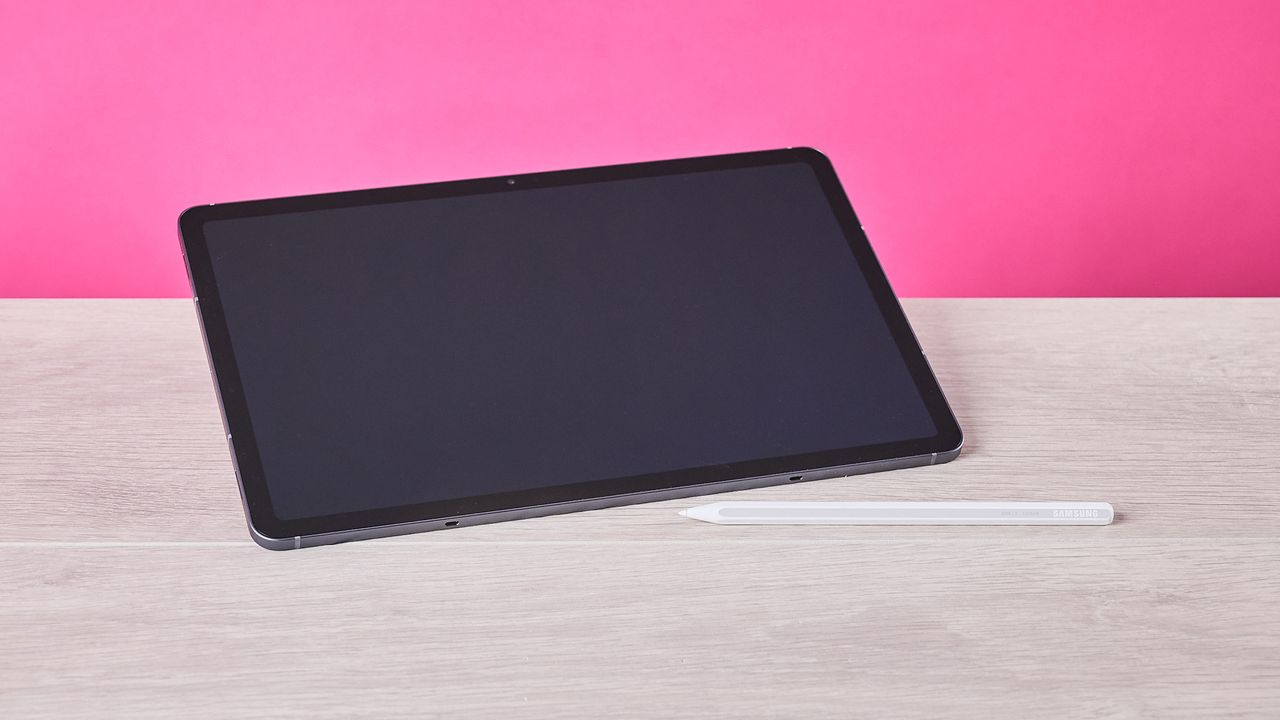 Three-quarter view of Samsung Galaxy Tab S11 and S Pen on a desk with pink wall in background