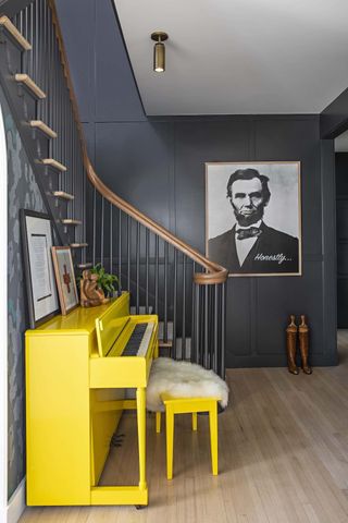 A bright yellow piano sits next to the bottom of a traditional staircase