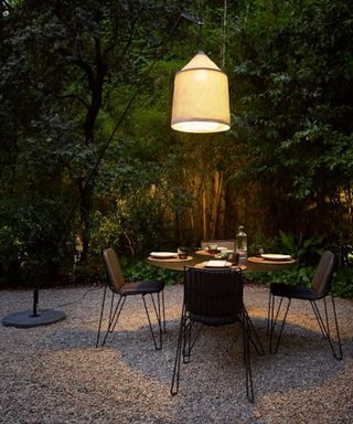 A gravel patio seating area with a black dining table and outdoor pendant light over the top