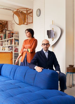 Designers Nipa Doshi and Jonathan Levien posing in their London Studio, next to a bright blue version of their Quilton Sofa for Hay