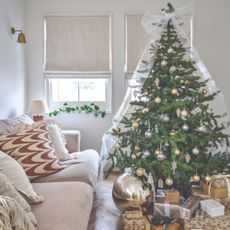 A white living room decorated for Christmas with a big tree adorned with a large white organza bow on the top